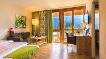 Helles Familienzimmer im Familienhotel Ramsi in Kärnten mit gemütlicher Sitzecke, Holzmöbeln und Balkon mit Blick auf die Berge