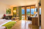 Helles Familienzimmer im Familienhotel Ramsi in Kärnten mit gemütlicher Sitzecke, Holzmöbeln und Balkon mit Blick auf die Berge