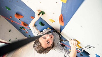 Teenager klettert die Kletterwand im Familienhotel hinauf.