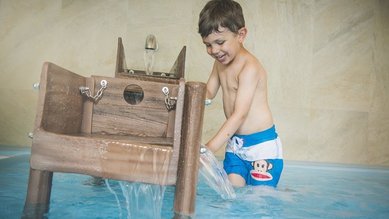 Ein Kind spielt im Hallenbad des Familienhotels Landgut Furtherwirt in Tirol an einem Wasserspiel im Becken.