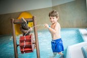 Junge spielt begeistert mit einer Wasserspritze im Kinderpool des Landguts Furtherwirt