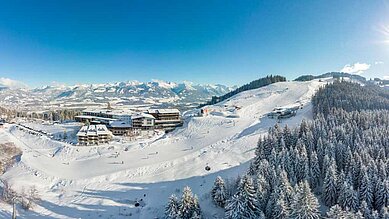 Luftaufnahme im Winter vom Hotelgelände und der Skipiste vom Familienhotel Allgäuer Berghof.