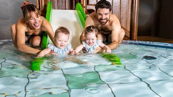 Eine junge Familie genießt gemeinsam das Plantschvergnügen im Babybecken des Familienhotels Das Bayrischzell in Oberbayern