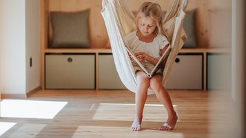Ein Mädchen sitzt während der Kinderbetreuung in einem hängenden Sessel im Hotel Bella Vista in Südtirol.