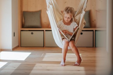 Ein Mädchen sitzt während der Kinderbetreuung in einem hängenden Sessel im Hotel Bella Vista in Südtirol.
