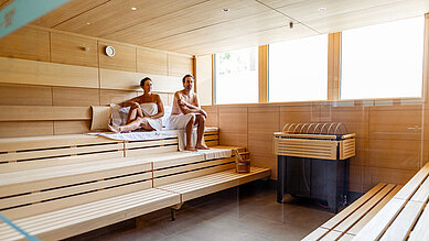 Zwei Gäste sitzen in der großen Sauna und genießen die Wellnesszeit im Familienhotel Das Bayrischzell in Oberbayern.
