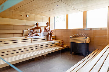 Zwei Gäste sitzen in der großen Sauna und genießen die Wellnesszeit im Familienhotel Das Bayrischzell in Oberbayern.