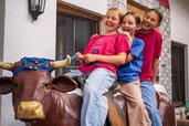 Drei lachende Kinder sitzen gemeinsam auf einer Spielkuh im Familienhotel Furtherwirt.