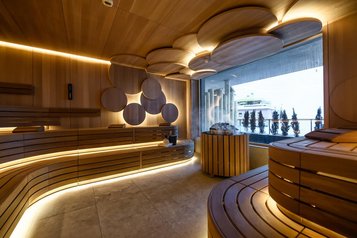 Modern gestaltete Sauna im Zauchenseehof mit runden Holzelementen, stimmungsvoller Beleuchtung und Blick nach draußen.