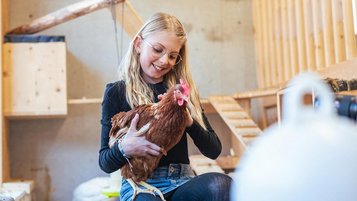 Mädchen streichelt ein Huhn im Familienhotel Almfamilyhotel Scherer in Tirol.