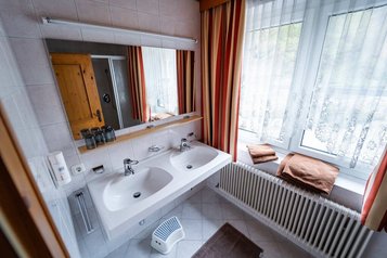 Helles Badezimmer im Familienhotel Bruckwirt mit Doppelwaschbecken, Spiegel und großen Fenstern.