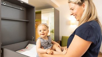 Kleinkind sitzt auf dem Wickeltisch im Familienzimmer im Kaiserhof und lacht gemeinsam mit der Mutter