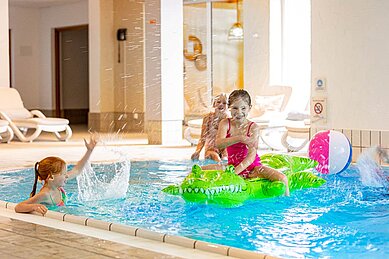 Mädchen planschen im Schwimmbad des Familienhotels Sonnenpark. Ein Mädchen sitzt auf einem Luft-Krokodil.