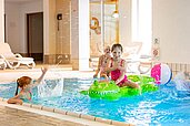 Mädchen planschen im Schwimmbad des Familienhotels Sonnenpark. Ein Mädchen sitzt auf einem Luft-Krokodil.
