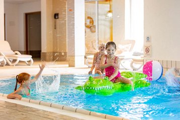 Mädchen planschen im Schwimmbad des Familienhotels Sonnenpark. Ein Mädchen sitzt auf einem Luft-Krokodil.