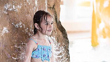 Mädchen steht im Pool des Familienhotels unter einem künstlichen Wasserfall