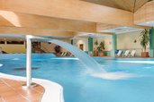 Innenpoolbereich des Familienhotels Sonnenhügel mit einer Wasserrutsche, umgeben von Liegestühlen und Pflanzendekorationen, unter einer hölzernen Deckenkonstruktion.