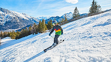 Junge fährt auf Skiern die weiße Piste hinab.