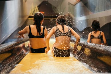 Drei Kinder rutschen in Badebekleidung gemeinsam eine Wasserrutsche im Familienhotel Alpenhotel Kindl hinunter.