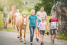 Eine Familie führt mit ihren Kindern die Pferde des Familienhotels Landgut Furtherwirt in Tirol aus.