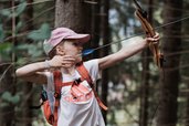 Ein Mädchen übt Bogenschießen im Wald beim Familienhotel Tirolerhof