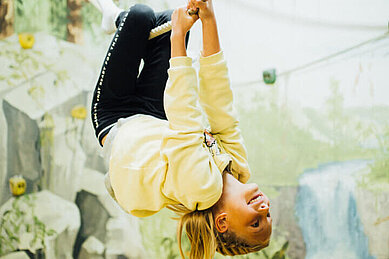 Mädchen klettert kopfüber an einem Seil im Happy-Club des Kinderhotels Sailer in Tirol.
