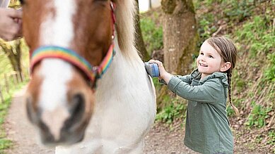 Ein Kind striegelt ein Pony im Familienurlaub.