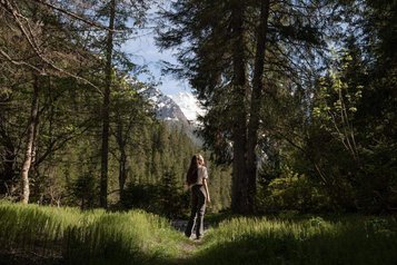 Eine Person wandert nahe dem Familienhotel Bella Vista in Südtirol durch den Wald mit Bergblick im Hintergrund.