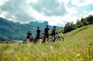 Familie unternimmt im Sommer eine Fahrradtour durch blühende Wiesen und Berge beim Familienhotel Post.