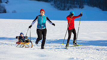 Mutter hat mit ihren beiden Kindern Spaß im Schnee im Winterurlaub in Vorarlberg.