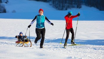 Mutter hat mit ihren beiden Kindern Spaß im Schnee im Winterurlaub in Vorarlberg.
