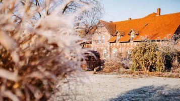 Historisches Backsteingebäude des Landhaus Averbeck an einem frostigen Wintermorgen, umgeben von gefrorenem Gras und winterlicher Bepflanzung.