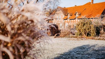 Historisches Backsteingebäude des Landhaus Averbeck an einem frostigen Wintermorgen, umgeben von gefrorenem Gras und winterlicher Bepflanzung.