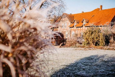Historisches Backsteingebäude des Landhaus Averbeck an einem frostigen Wintermorgen, umgeben von gefrorenem Gras und winterlicher Bepflanzung.