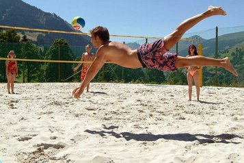 Familie spielt auf dem Volleyballplatz an einem Sommertag Volleyball und genießen den Aufenthalt im Familienhotel Sonngastein in Bad Gastein.