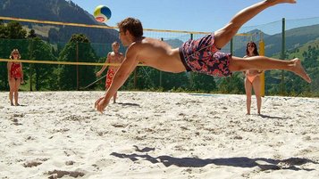 Familie spielt auf dem Volleyballplatz an einem Sommertag Volleyball und genießen den Aufenthalt im Familienhotel Sonngastein in Bad Gastein.