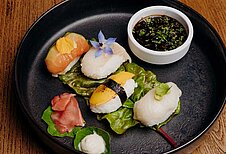 Ein fein angerichteter Teller mit einer Auswahl an Maki-Sushi, garniert mit frischen Blumen und Blättern, serviert mit einer Schale Sojasauce im Hotel Habachklause.