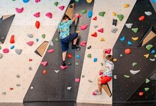 Zwei Jungen in Freizeitkleidung klettern konzentriert an einer farbenfrohen Boulderwand mit Griffen in verschiedenen Formen im Familienhotel Amiamo.