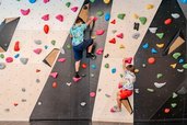 Zwei Jungen in Freizeitkleidung klettern konzentriert an einer farbenfrohen Boulderwand mit Griffen in verschiedenen Formen im Familienhotel Amiamo.