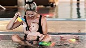 Ein Baby sitzt mit seiner Mutter im Pool des Familienhotel Mia Alpina in Tirol und spielt mit buntem Wasserspielzeug.
