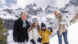 Winter im Salzburger Land: Familie macht mit Opa eine Winterwanderung in Filzmoos. Im Hintergrund ein eindrucksvolles Bergpanorama.