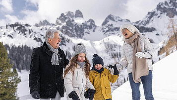 Winter im Salzburger Land: Familie macht mit Opa eine Winterwanderung in Filzmoos. Im Hintergrund ein eindrucksvolles Bergpanorama.