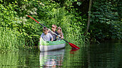 Drei Kindern rudern in einem Kanu auf dem Fluss des Kinderhotels Bruckwirt in Oberösterreich.