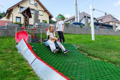 Kinder beim Rutschen auf grüner Outdoor-Bahn auf der Wiese des Hotel Engel im Schwarzwald