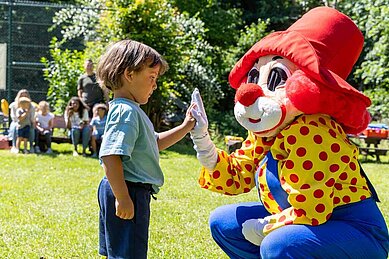 Kleiner Junge gibt Maskottchen Happy ein High Five im Family Club Harz