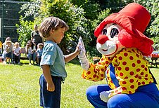 Kleiner Junge gibt Maskottchen Happy ein High Five im Family Club Harz