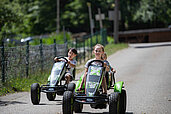 Zwei Kinder fahren ein Kartrennen auf dem Hof im Kinderhotel Bruckwirt in Oberösterreich.