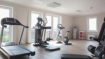 Ein helles und geräumiges Fitnessstudio im Familienhotel Deichkrone mit einer Auswahl an Trainingsgeräten wie Laufband, Ellipsentrainer, Fahrrad und Gewichtsbank.