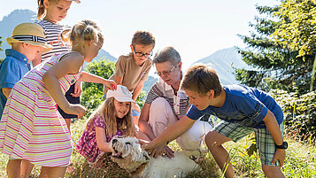 Kinder streicheln Hund in der Wiese im Familienurlaub im Kaiserhof in Tirol.