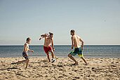 Kinder des Familienhotels Seeklause spielen mit Ihrem Vater an der Ostsee am Strand Fußball.